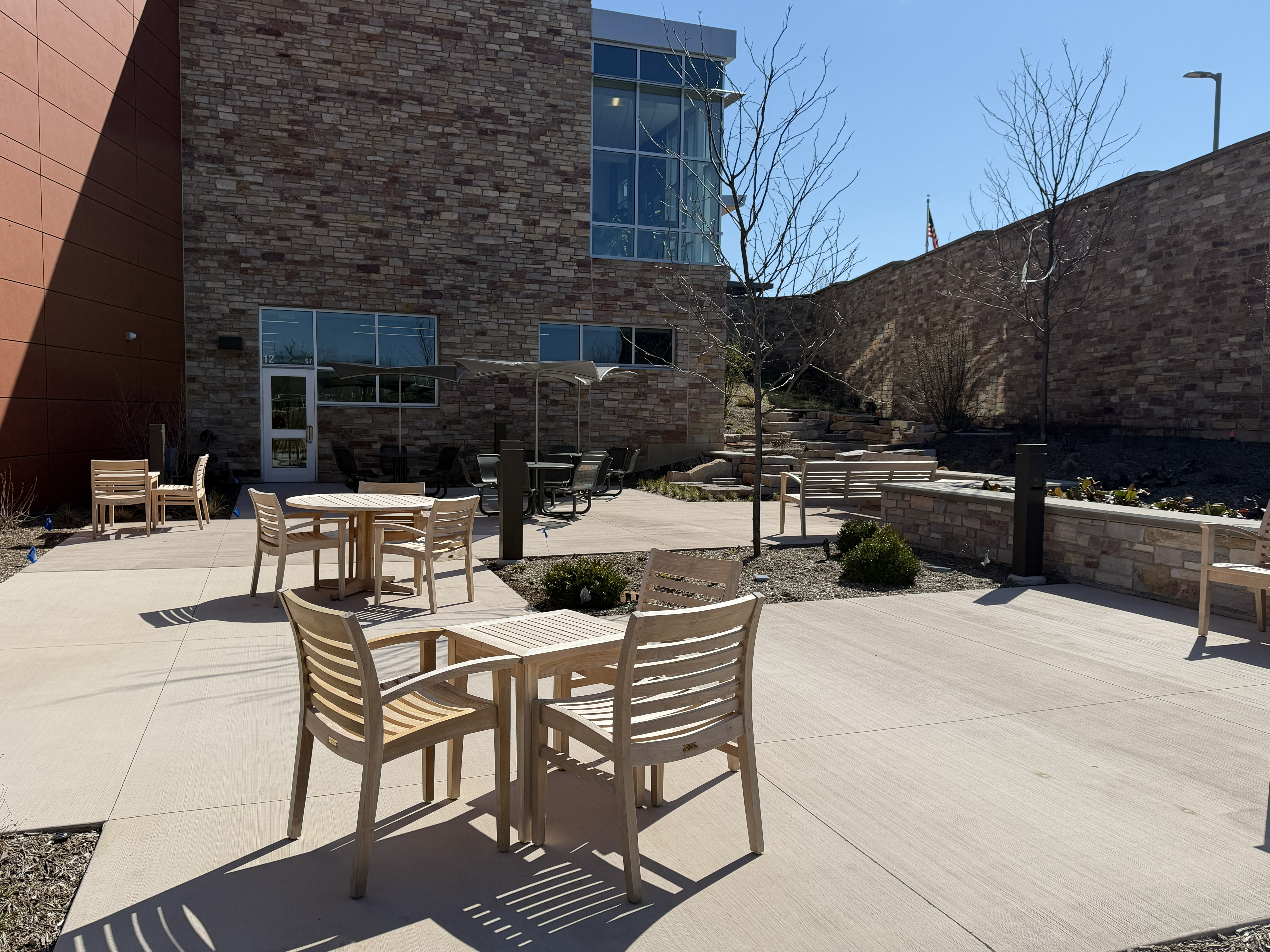 A picture of the outdoor reading room featturing wood tables and chairs and rock water fountain