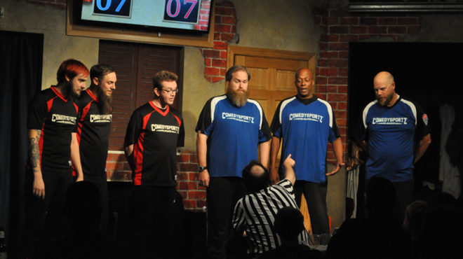 picture of 6 people on a stage wearing colored uniform.  Three in black and three in blue.