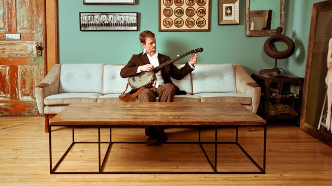 Photograph of a man playing a banjo on a couch